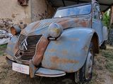 rusted old car parked in front of a building with a roof over it