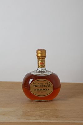 une bouteille de whisky posée sur une table en bois, avec un mur blanc en arrière-plan