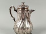 une cafetière ancienne en argent, posée sur un socle et munie d'un couvercle