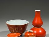 Trois vases rouges, un bol et une tasse sont posés sur une table.