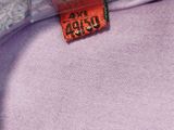 purple shirt with a red tag on it sitting on top of a bed