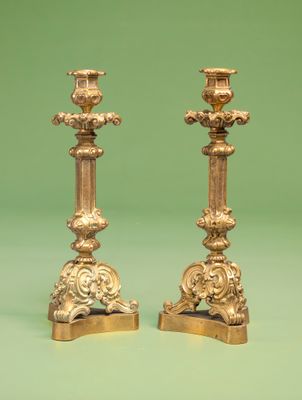 une paire de bougeoirs anciens en laiton posés sur un socle, sur fond vert