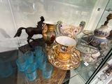 une vitrine en verre contenant une figurine de cheval ainsi qu'une tasse et une soucoupe