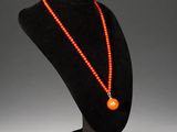 an orange beaded necklace on a black mannequin stand