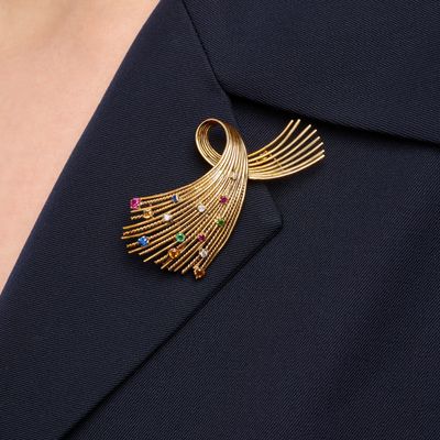 a close up of a woman wearing a gold brooch with multi colored stones