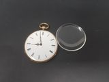 an image of a pocket watch and a magnifying lens on a black surface