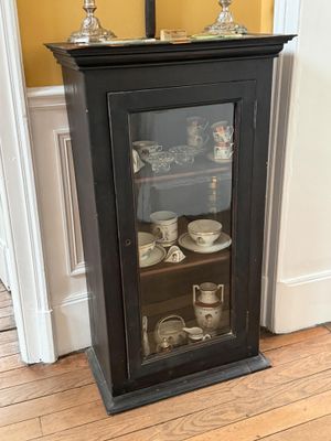 une armoire noire avec une porte vitrée, dans un coin de la pièce