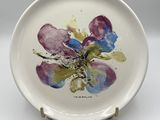 une assiette blanche sur laquelle est peinte une fleur violette et bleue