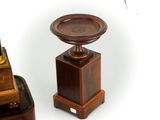 a small clock on a pedestal next to a smaller clock on a table