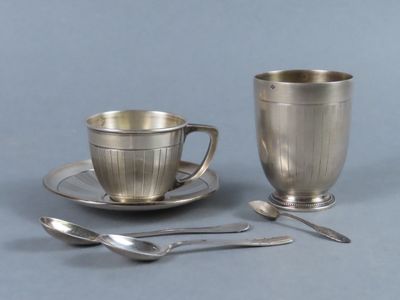 une tasse et une soucoupe en argent, avec des cuillères à côté
