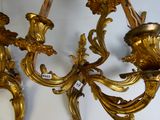 two gold colored sconces hanging on a wall next to a mirror
