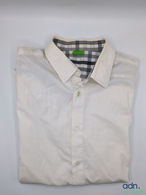 La chemise est blanche et possède un col à carreaux.