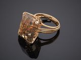 a yellow gold ring with a square cut diamond on a black surface