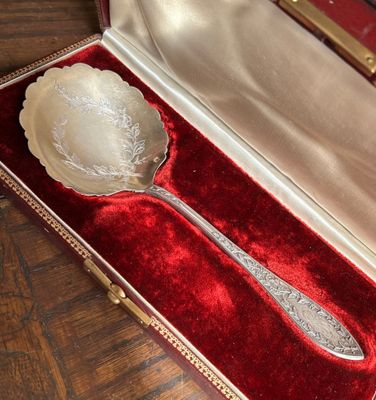 une cuillère en argent dans un étui en velours rouge, posée sur une table en bois