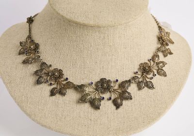 une photo d'un collier porté par un mannequin, orné de fleurs et de feuilles