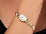 une femme portant au poignet un bracelet en or avec un cadran blanc