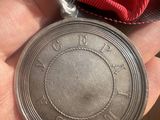 someone is holding a silver medal with a red ribbon around it
