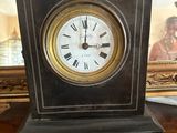 une petite horloge posée sur une table, avec un tableau en arrière-plan