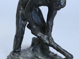 statue représentant un homme penché en avant pour ramasser quelque chose par terre