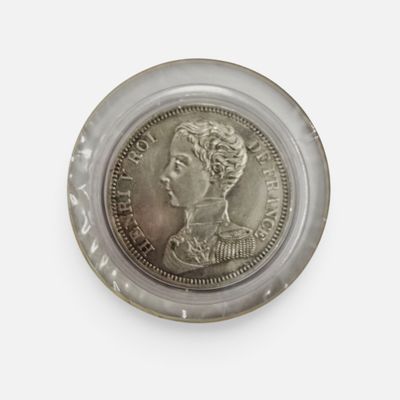 une pièce d'argent dans un récipient en verre posé sur une surface blanche