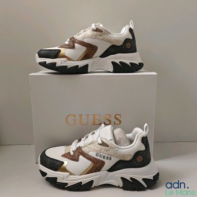 une paire de baskets blanches et dorées exposées dans une boîte