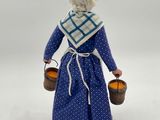 figurine of a woman in a blue dress holding two buckets of oranges