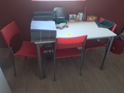 une table blanche avec des chaises rouges et une pile de papiers posée dessus