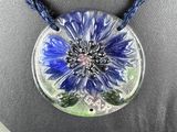 purple and blue flower pendant on a black necklace on a mannequin
