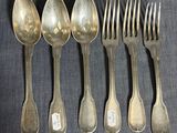 six cuillères en argent et une fourchette sont alignées sur une table