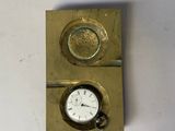 une petite horloge posée sur un plateau doré, sur une table blanche
