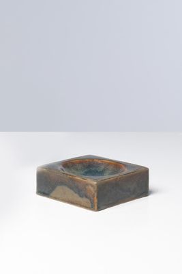 un petit cendrier carré en céramique posé sur une surface blanche