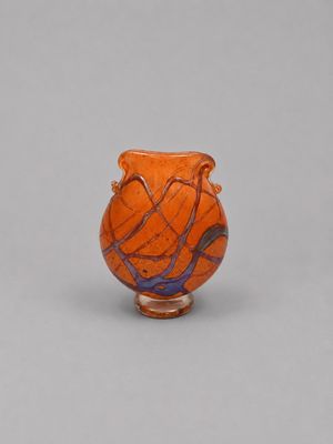 un vase orange posé sur une table blanche, près d'un mur gris