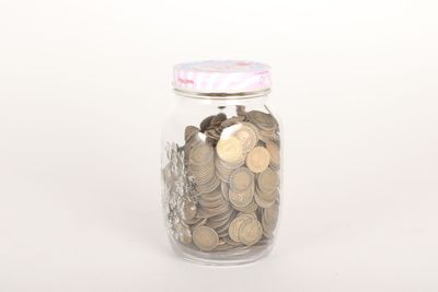 un bocal en verre rempli de pièces de monnaie posé sur une surface blanche