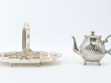 two silver teapots and a tray on a white surface