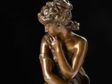 bronze statue of a woman sitting on a rock with her hand on her chin