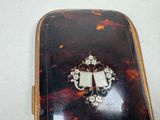 a tortoise shell case with a silver broocher on it