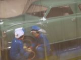 two men working on a green toy car in a display case