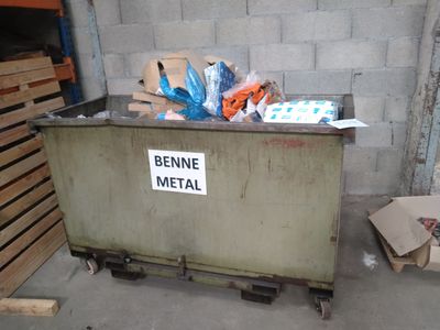 une benne à ordures sur laquelle est accrochée une pancarte, dans un immeuble