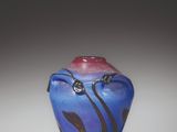 un vase bleu surmonté d'un couvercle rouge, posé sur une surface blanche