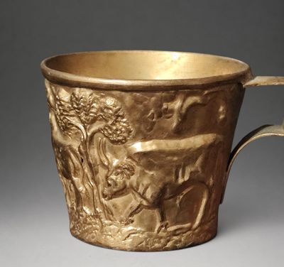 a gold cup with a design of animals and people on it