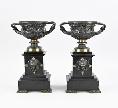 paire de vases noirs et dorés ornés de têtes de lion, posés sur des socles