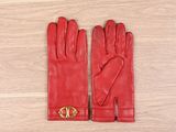 des gants en cuir rouge ornés de boucles dorées, posés sur un parquet
