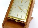 une petite horloge en bois posée sur un socle, sur une surface blanche