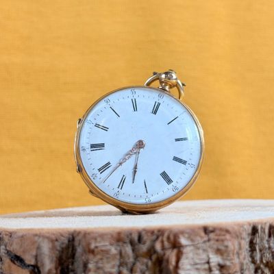 a gold pocket watch sitting on top of a piece of wood