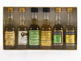 six petites bouteilles de whisky dans un coffret en bois, posées sur une surface blanche