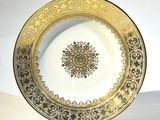 une assiette dorée et blanche posée sur un support, sur une surface blanche