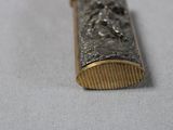 a small silver and gold object on a white surface