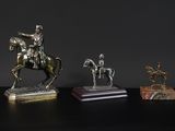 three bronze statues of men on horses on a black surface