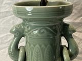 a green vase with a lamp on top of it