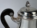 a silver coffee pot with a black handle on a table